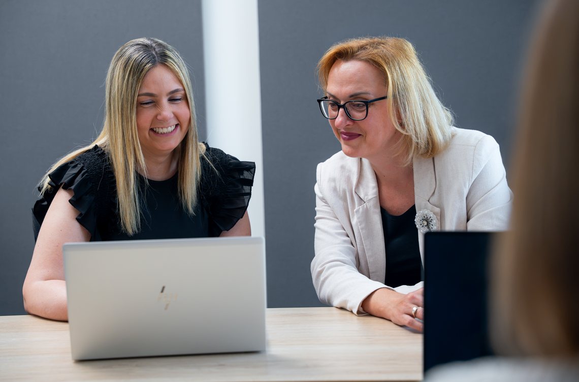Zwei Kolleginnen lachen gemeinsam am Laptop